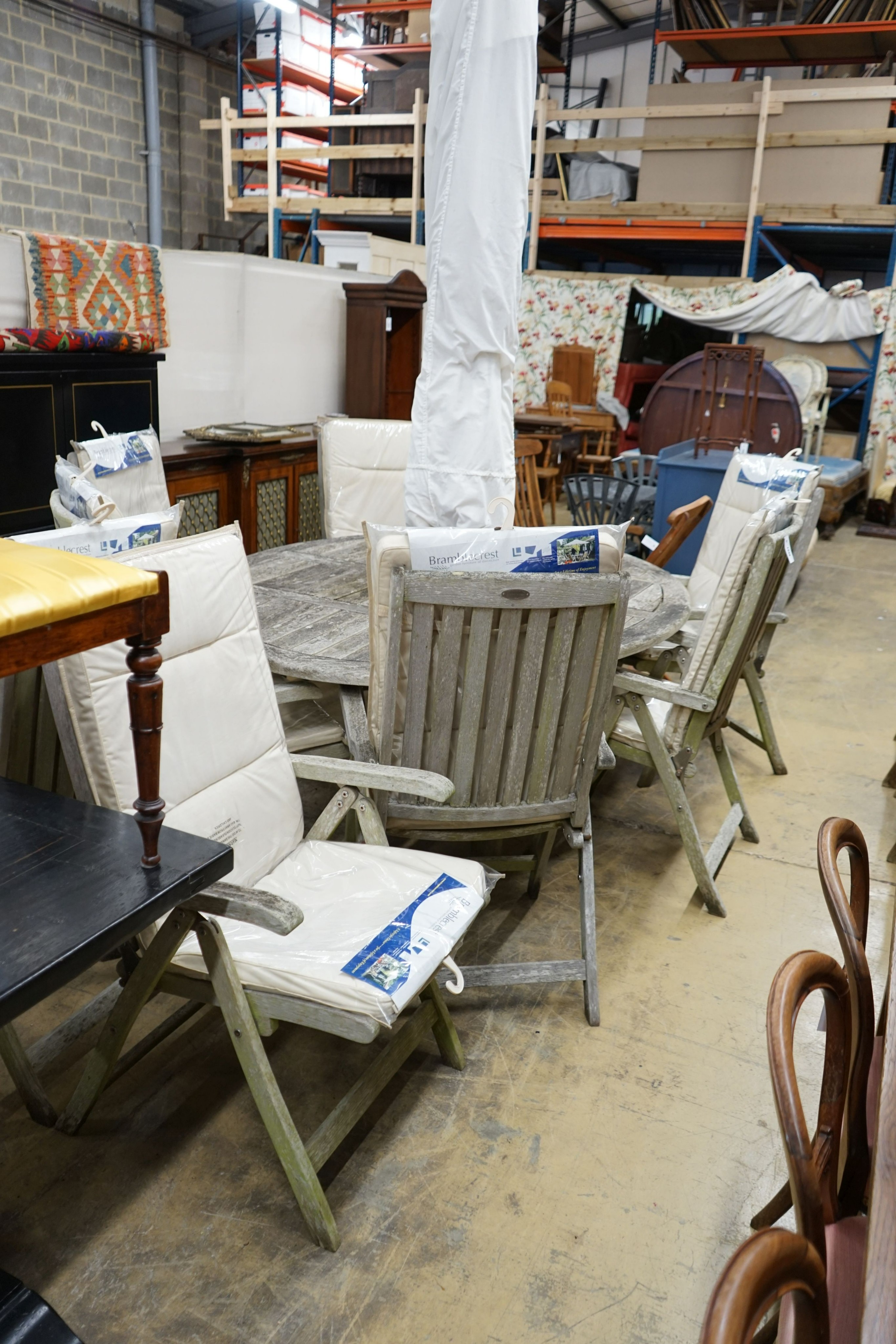 A Bramblecrest weathered teak oval garden table, width 200cm, depth 150cm, height 74cm eight folding teak reclining elbow chairs, seat pads and parasol with stone base